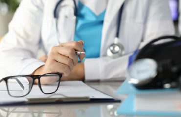 Close-up of doctor workplace with notebook and glasses. Professional specialist in medical gown sitting at table. Physician working at hospital. Medicine and healthcare concept